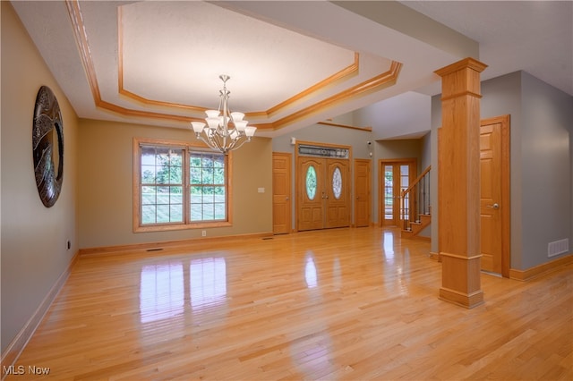 interior space featuring a tray ceiling, an inviting chandelier, decorative columns, and light hardwood / wood-style floors