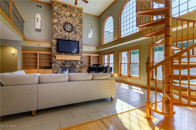 living room featuring hardwood / wood-style floors, a stone fireplace, ceiling fan, ornamental molding, and a towering ceiling