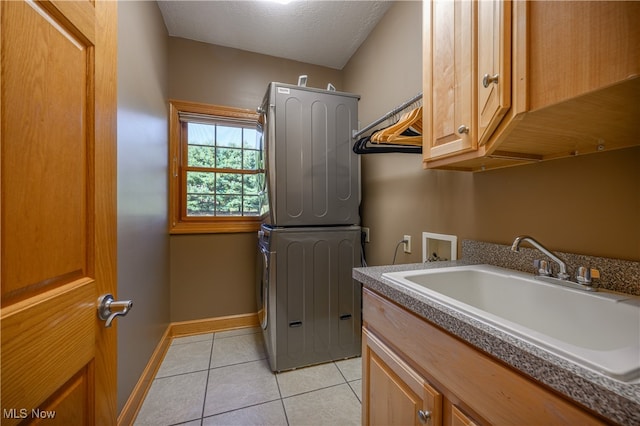 laundry room with cabinets, stacked washer and dryer, a textured ceiling, light tile patterned floors, and sink