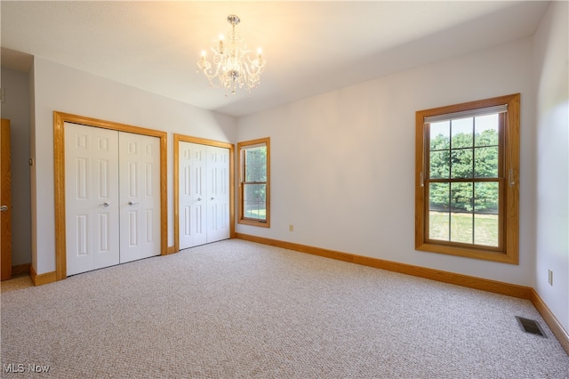 unfurnished bedroom with an inviting chandelier, two closets, and carpet floors