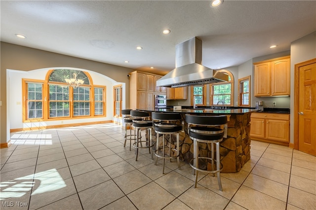 kitchen featuring a textured ceiling, island exhaust hood, a kitchen bar, kitchen peninsula, and light tile patterned flooring