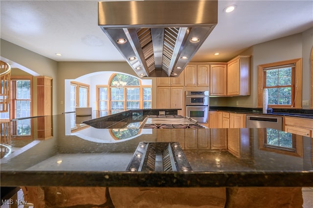 kitchen featuring dark stone countertops, island range hood, a wealth of natural light, and appliances with stainless steel finishes