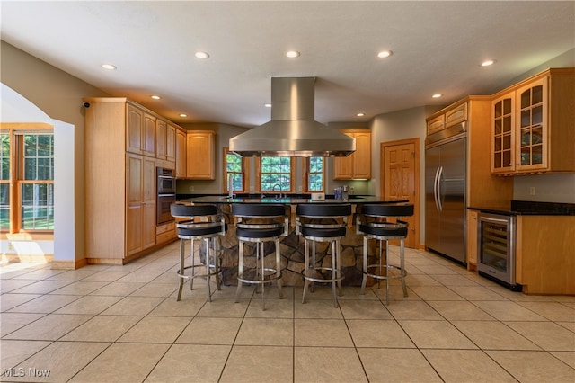 kitchen featuring built in refrigerator, island range hood, wine cooler, and a breakfast bar