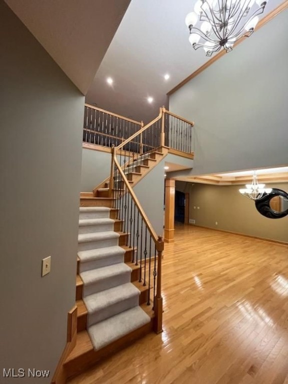 stairway with a towering ceiling, a chandelier, and hardwood / wood-style flooring