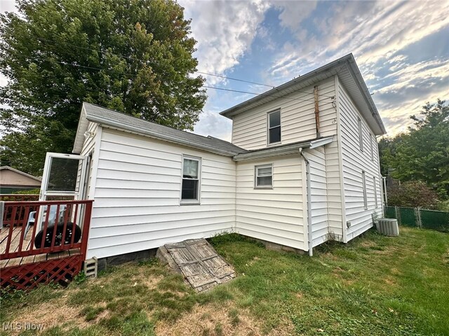 back of house featuring cooling unit, a wooden deck, and a lawn