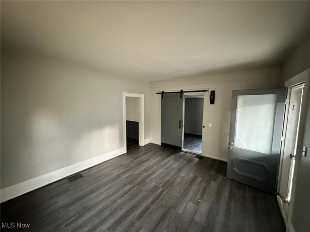 unfurnished bedroom with dark hardwood / wood-style flooring, a barn door, and a closet