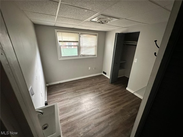 unfurnished bedroom with a closet, hardwood / wood-style floors, and a drop ceiling