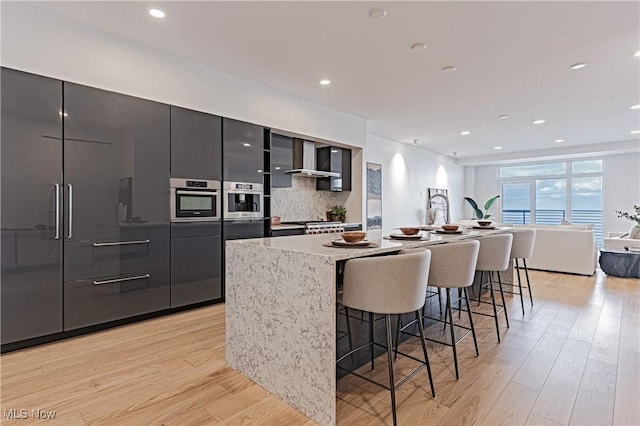 kitchen featuring a center island with sink, a breakfast bar, wall chimney exhaust hood, and tasteful backsplash