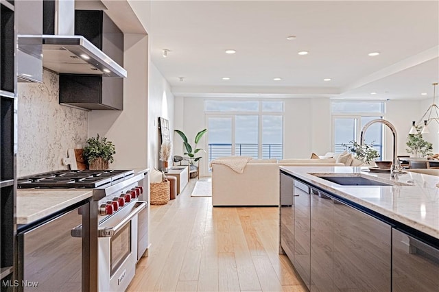 kitchen with tasteful backsplash, light stone counters, wall chimney exhaust hood, designer range, and sink