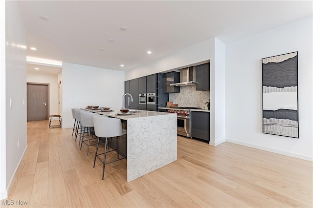 kitchen with wall chimney exhaust hood, tasteful backsplash, an island with sink, a breakfast bar area, and high end stainless steel range