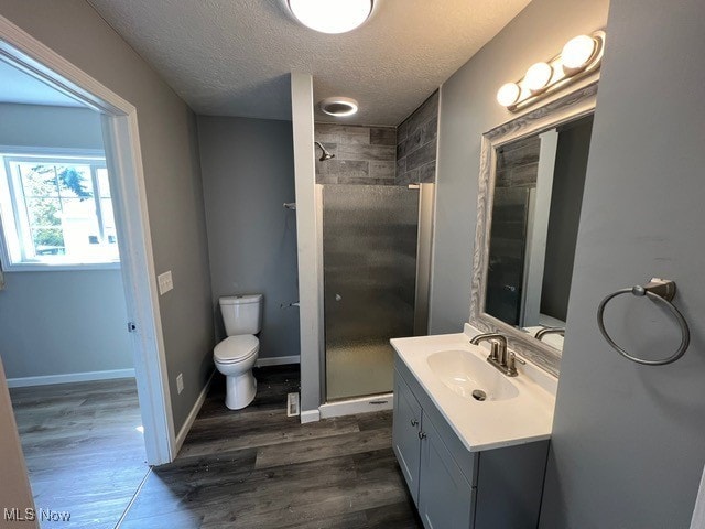 bathroom featuring vanity, a textured ceiling, hardwood / wood-style flooring, a shower with door, and toilet