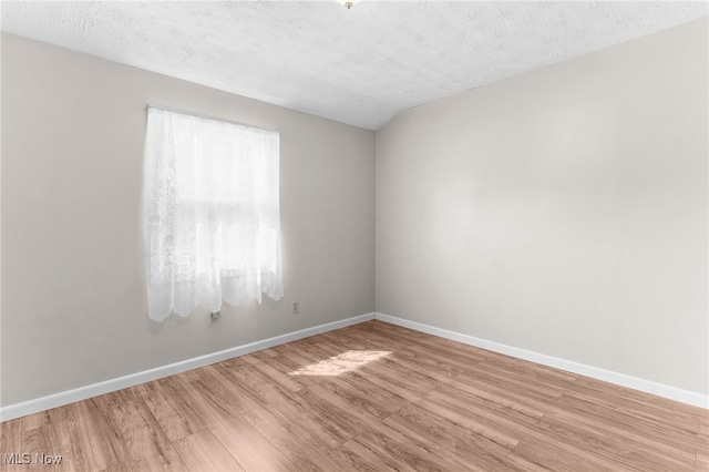 spare room with lofted ceiling, wood-type flooring, and a textured ceiling