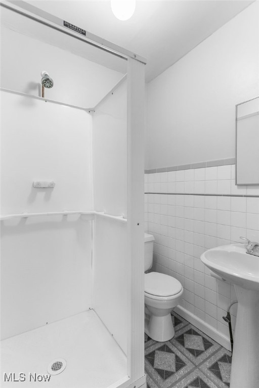 bathroom featuring a shower, tile walls, tile patterned flooring, and toilet