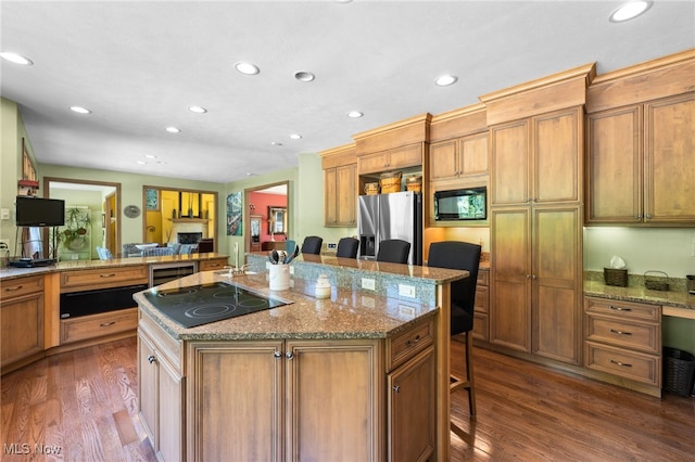 kitchen featuring light stone counters, black appliances, dark hardwood / wood-style floors, a breakfast bar area, and a kitchen island