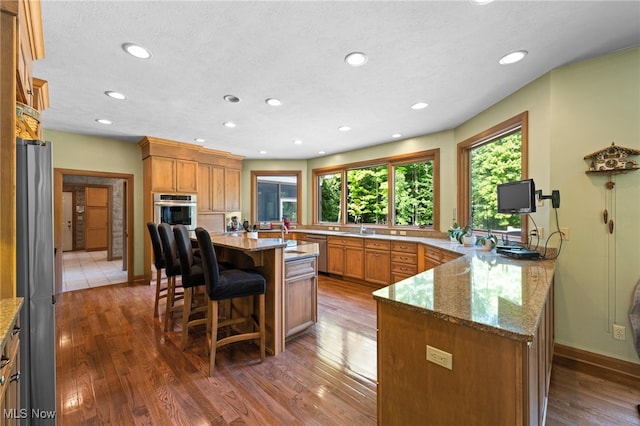 kitchen featuring a center island with sink, dark hardwood / wood-style floors, light stone countertops, and appliances with stainless steel finishes