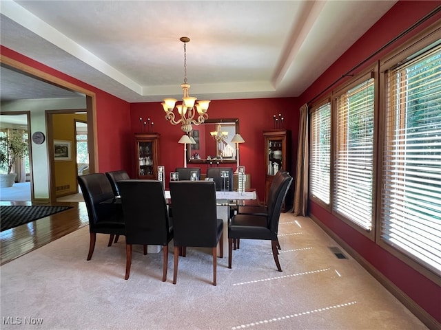 carpeted dining room with a tray ceiling and a chandelier