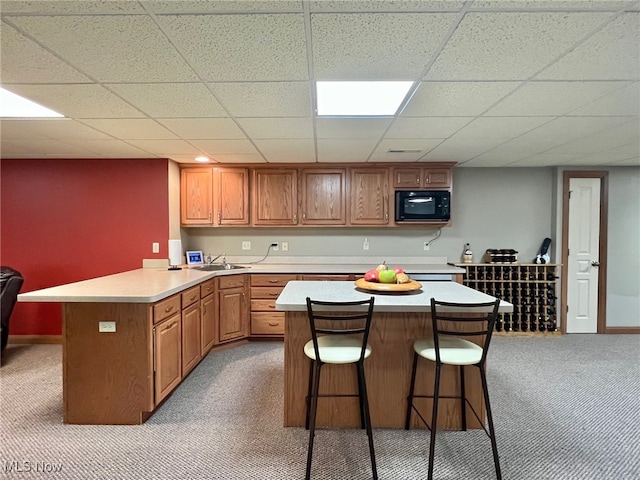 kitchen featuring a paneled ceiling, a kitchen breakfast bar, a center island, and light carpet