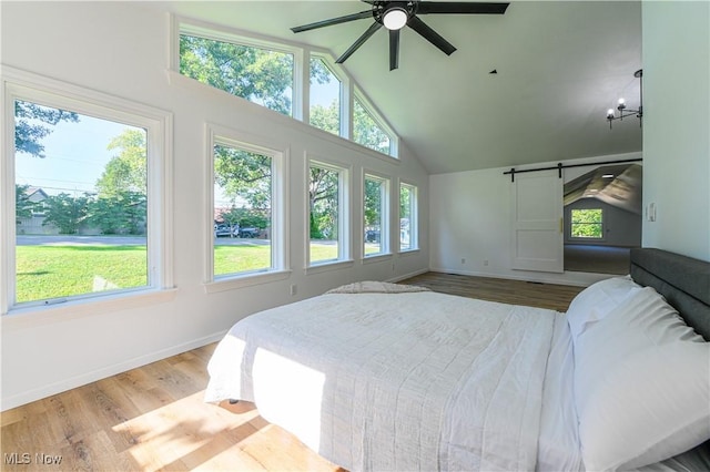 bedroom featuring hardwood / wood-style floors, ceiling fan with notable chandelier, a barn door, and lofted ceiling