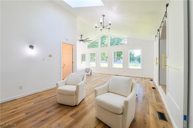 sitting room featuring ceiling fan with notable chandelier, light wood-type flooring, a skylight, and high vaulted ceiling