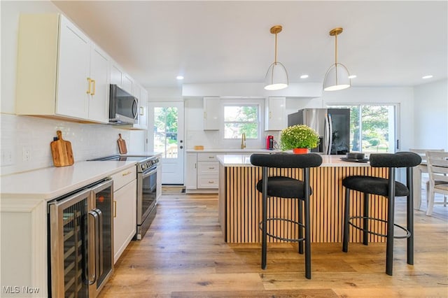 kitchen with appliances with stainless steel finishes, a kitchen island, a healthy amount of sunlight, light hardwood / wood-style floors, and wine cooler