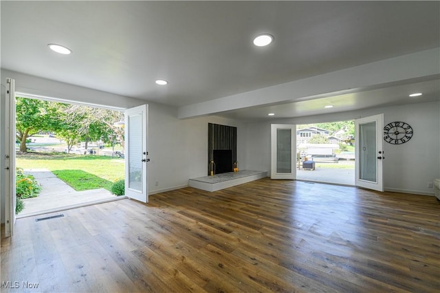 unfurnished living room featuring a tile fireplace, french doors, and dark wood-type flooring