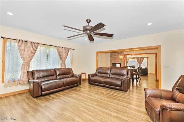 living room with light wood-type flooring, ceiling fan, and a brick fireplace