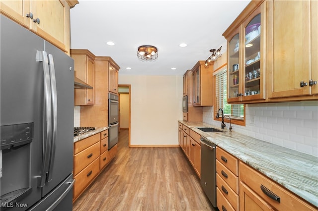 kitchen with light wood-type flooring, light stone counters, stainless steel appliances, and sink