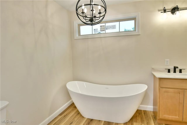 bathroom with toilet, a tub, a notable chandelier, vanity, and hardwood / wood-style flooring