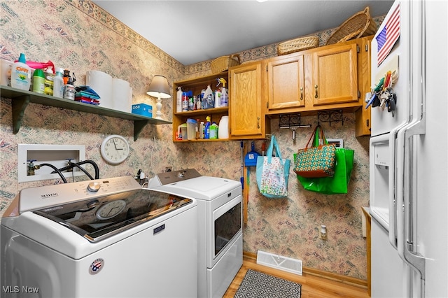 clothes washing area with independent washer and dryer, cabinets, and light wood-type flooring