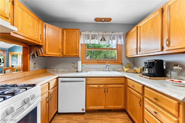 kitchen featuring light wood-type flooring, white appliances, hanging light fixtures, and sink