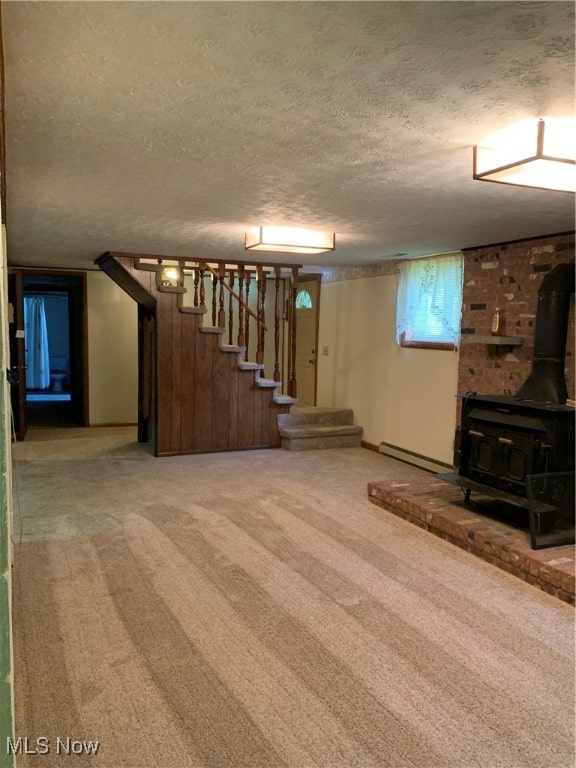 basement featuring a textured ceiling, a baseboard radiator, carpet flooring, and a wood stove