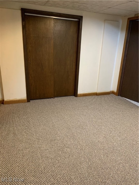 unfurnished bedroom featuring a drop ceiling, carpet, and a closet