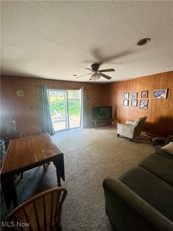 living room featuring a textured ceiling, ceiling fan, wood walls, and carpet floors