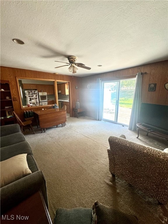 carpeted living room with a textured ceiling, ceiling fan, and wooden walls