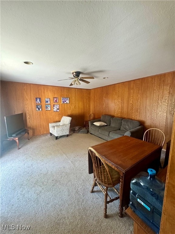 carpeted dining space featuring a textured ceiling, ceiling fan, and wooden walls