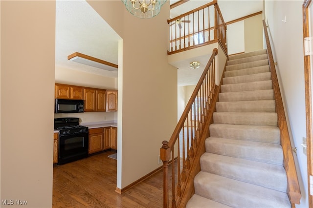 staircase with a high ceiling, hardwood / wood-style flooring, and a notable chandelier