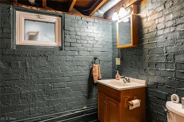 bathroom featuring toilet, brick wall, and vanity