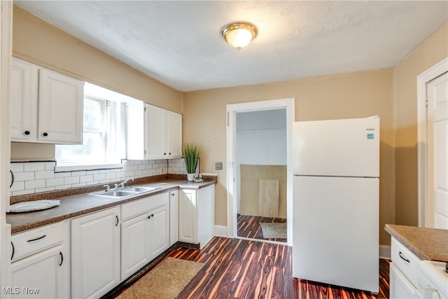 kitchen with white cabinets, backsplash, sink, white fridge, and dark wood-type flooring