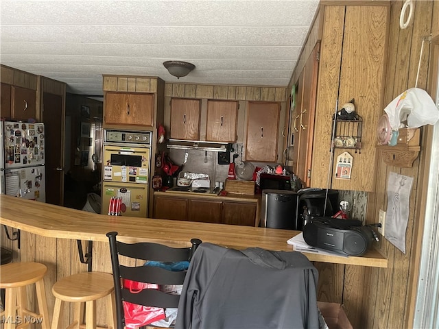 kitchen featuring wood walls, stainless steel fridge, kitchen peninsula, and a breakfast bar