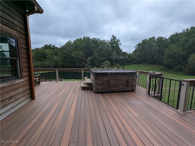 wooden terrace with a hot tub, a forest view, and a lawn