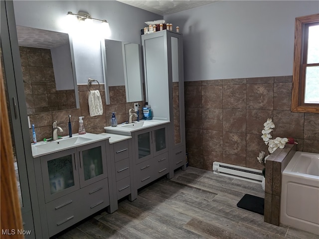 bathroom featuring tile walls, vanity, a tub, hardwood / wood-style floors, and a baseboard heating unit