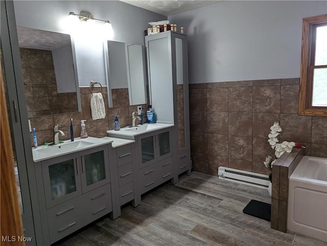 bathroom featuring tile walls, baseboard heating, a sink, and wood finished floors
