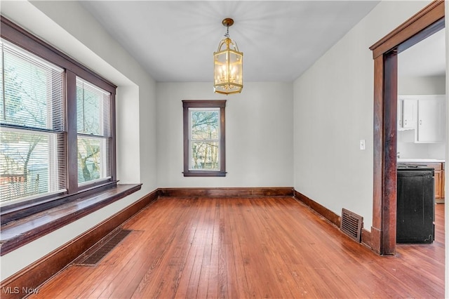 unfurnished dining area with light hardwood / wood-style floors, a wealth of natural light, and an inviting chandelier