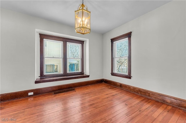 unfurnished room featuring wood-type flooring and an inviting chandelier