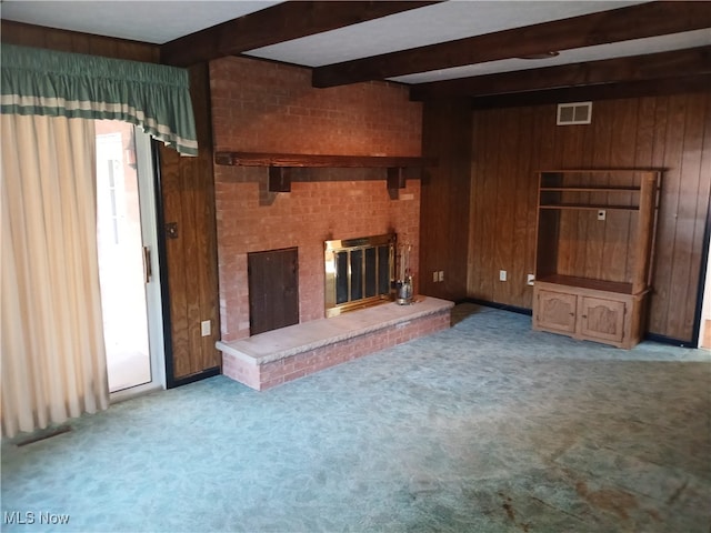 unfurnished living room featuring light carpet, beamed ceiling, a fireplace, and wooden walls