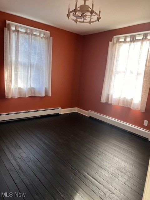 unfurnished room featuring a baseboard radiator, baseboards, an inviting chandelier, and dark wood finished floors