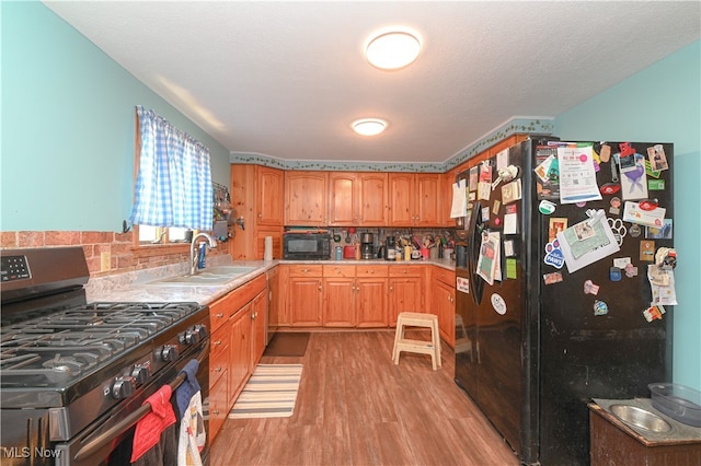 kitchen with light hardwood / wood-style floors, backsplash, a textured ceiling, black appliances, and sink