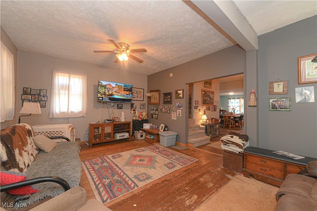 living room with a textured ceiling, ceiling fan, and light hardwood / wood-style flooring