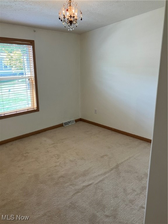 spare room with light colored carpet, an inviting chandelier, and a textured ceiling