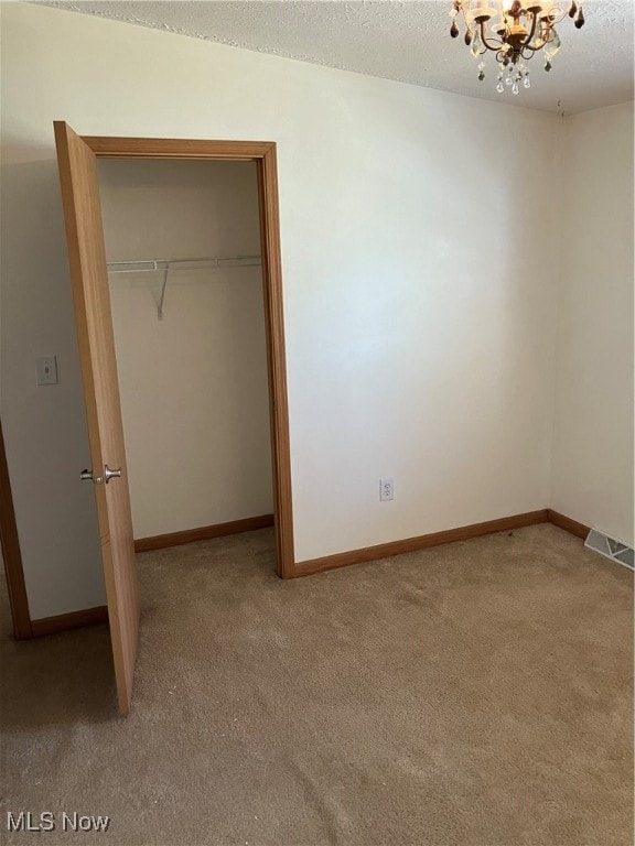 unfurnished bedroom with light carpet, a closet, a notable chandelier, and a textured ceiling